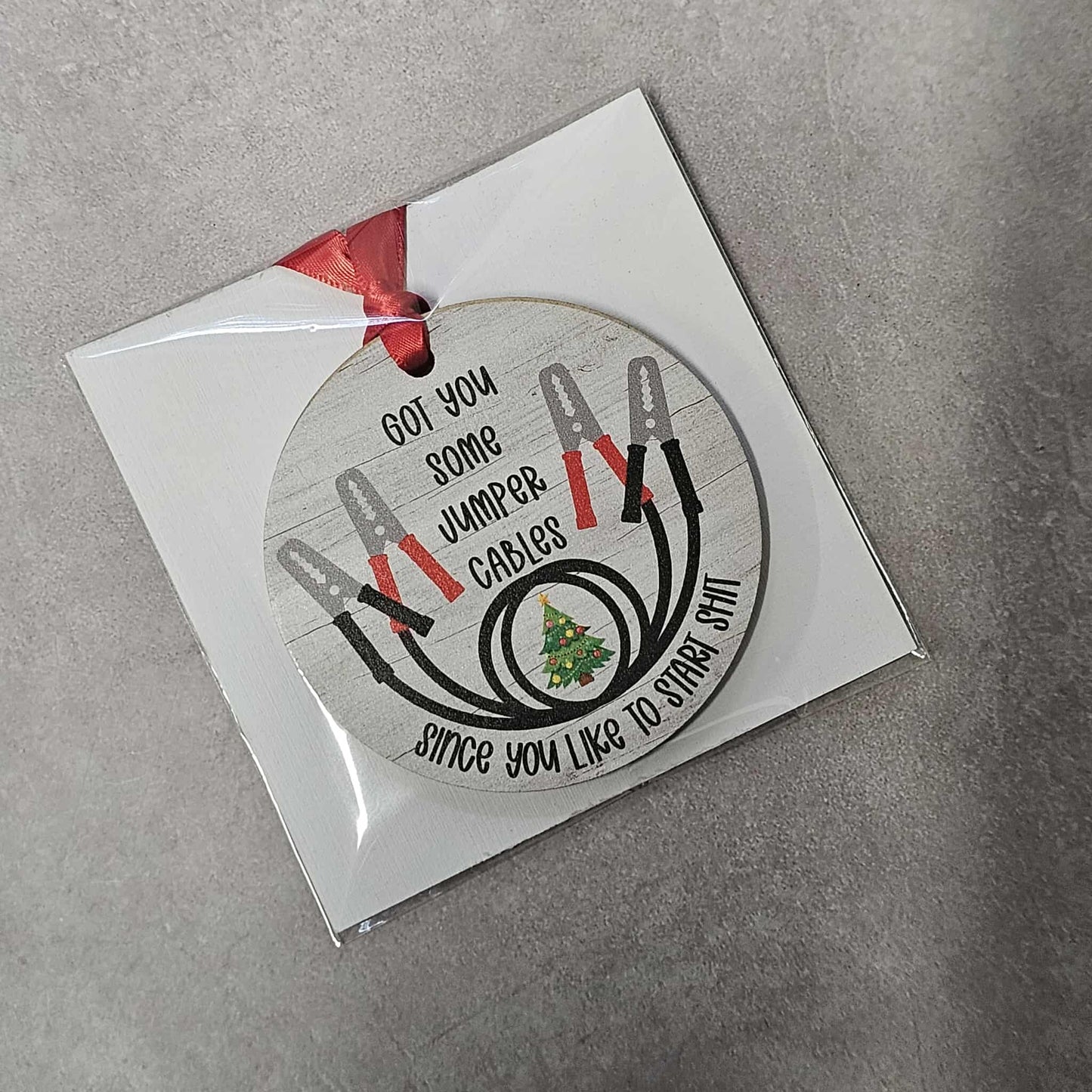 Round Christmas ornament with jumper cables and text on a gray background