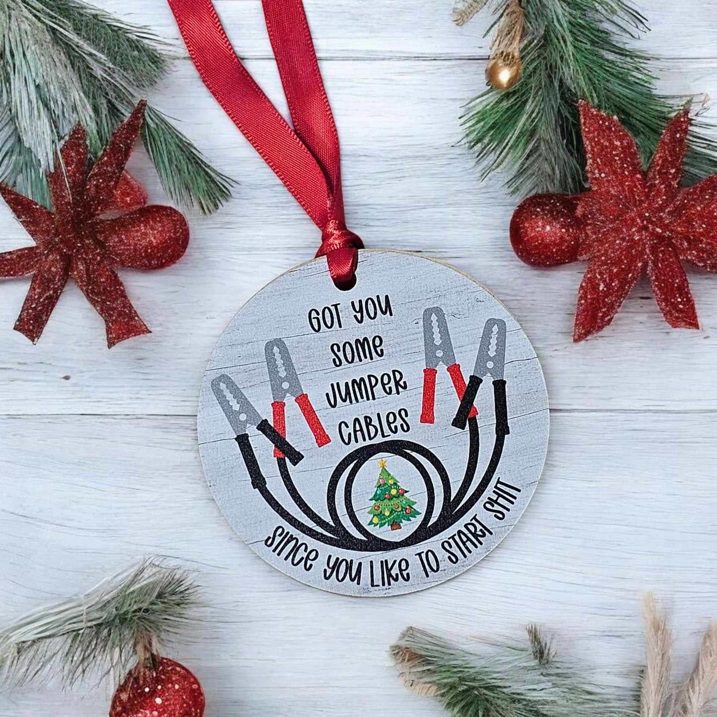 Decorative Christmas ornament with jumper cables design and text on a wooden background.
