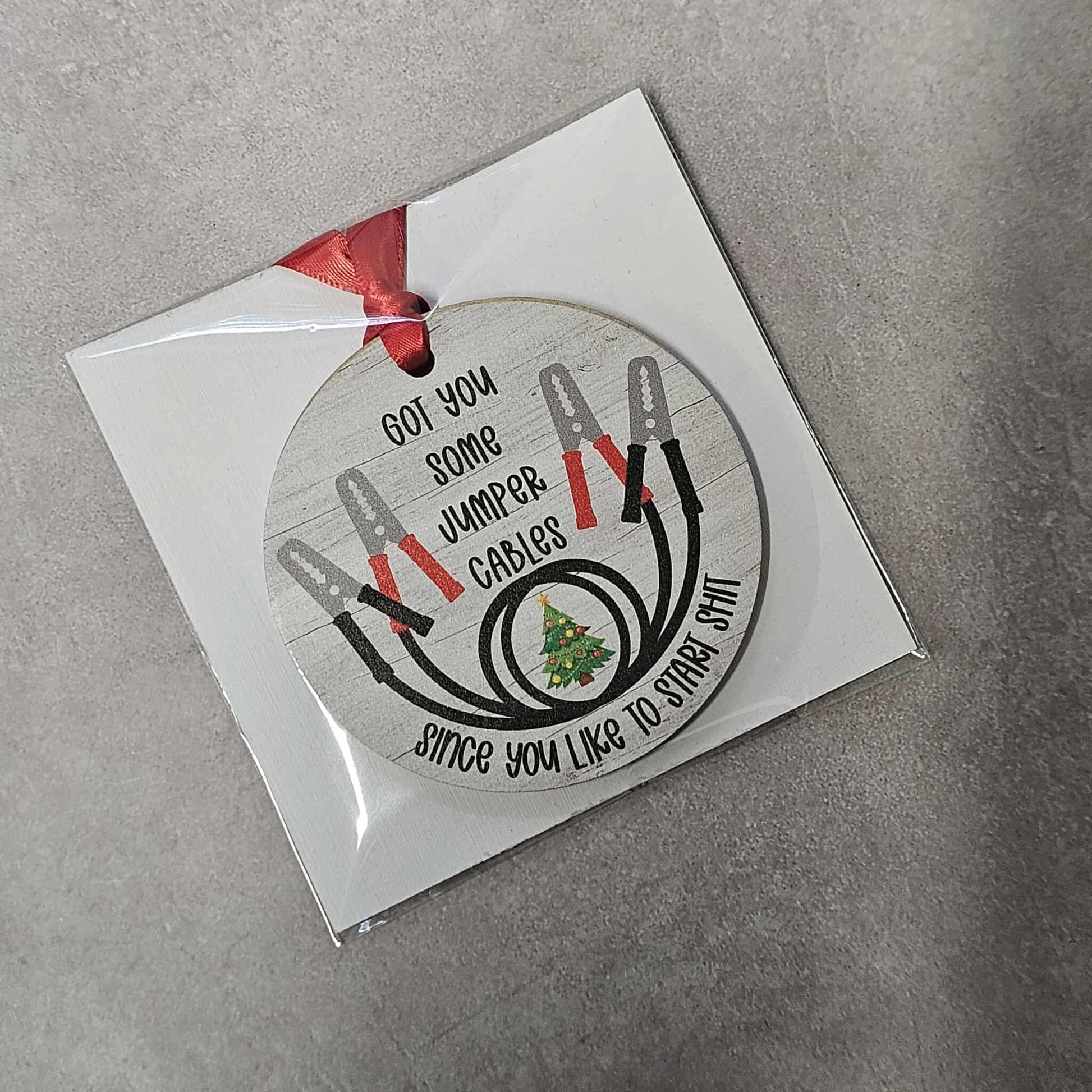Round Christmas ornament with jumper cables and text on a gray background