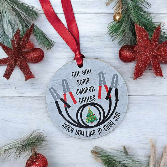 Decorative Christmas ornament with jumper cables design and text on a wooden background.
