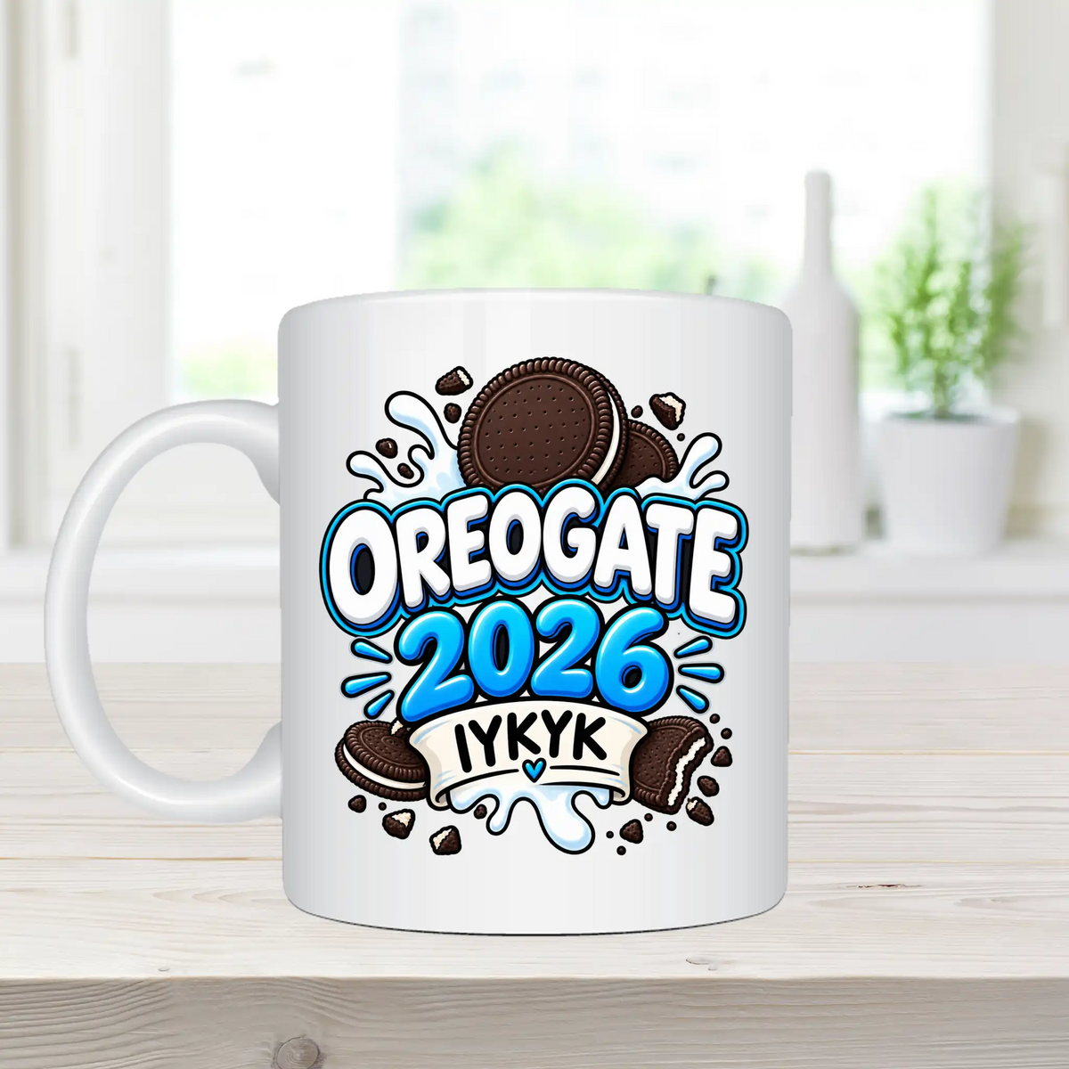 A white ceramic mug with a colorful 'OREOGATE 2026 IYKYK' graphic featuring cookies, placed on a light wooden surface with a blurred kitchen background.