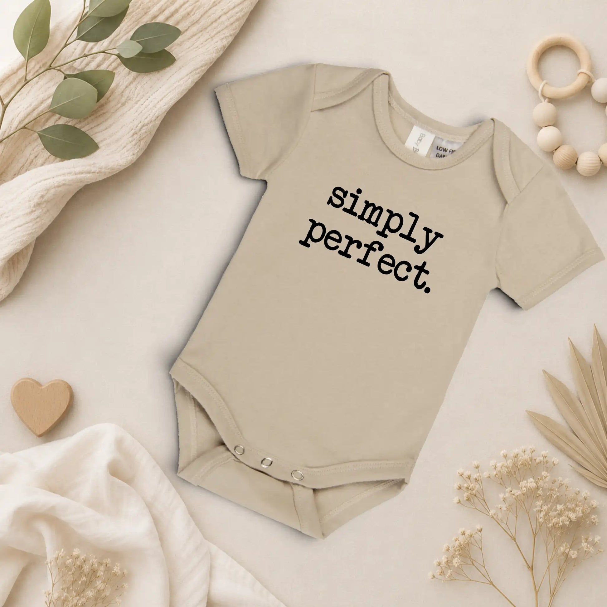 Beige baby onesie with 'simply perfect' text on a neutral background with decorative elements.